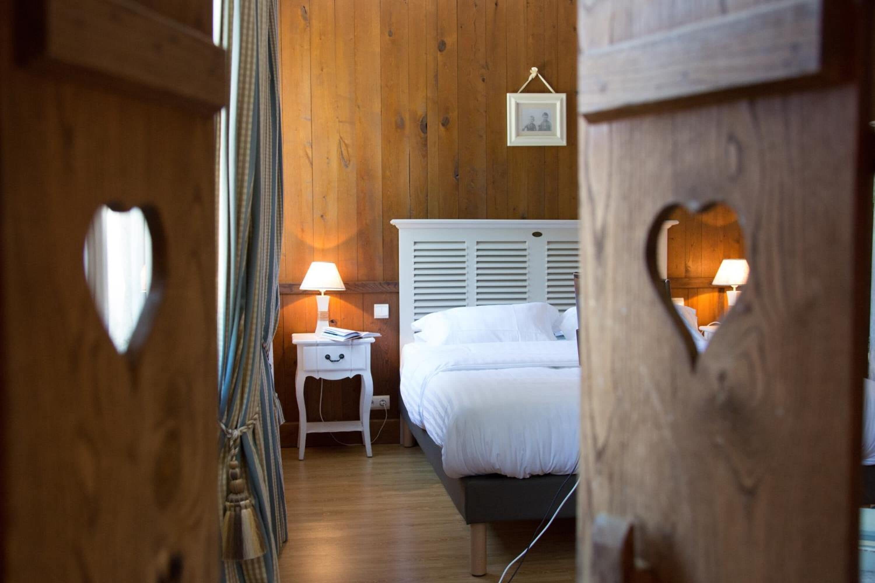Un dormitorio con pared de madera, una cama blanca con cabecera y dos lámparas de noche.