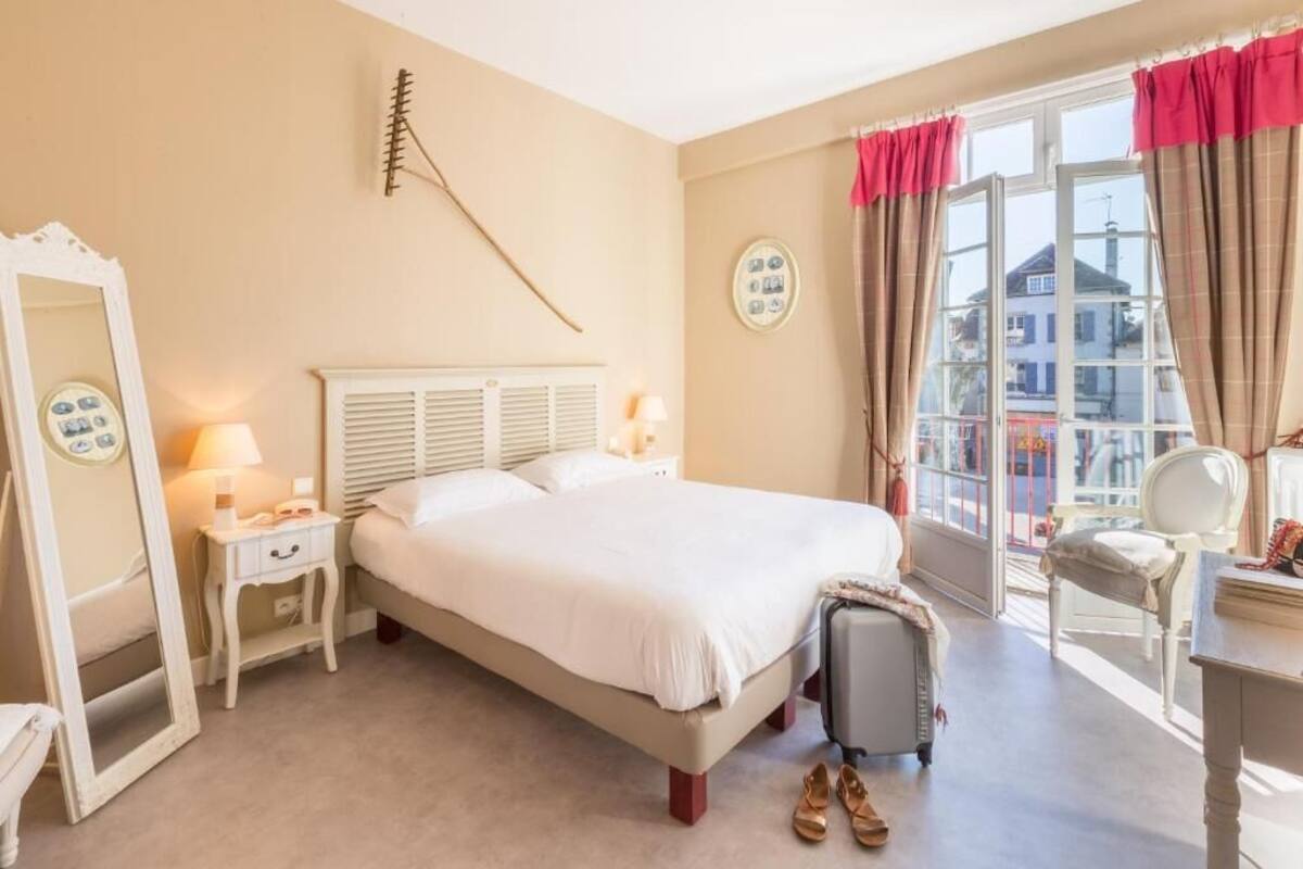 Ein Hotelzimmer mit Bett, Nachttischen, einem Spiegel, einem Koffer und einem Fenster mit Vorhängen.