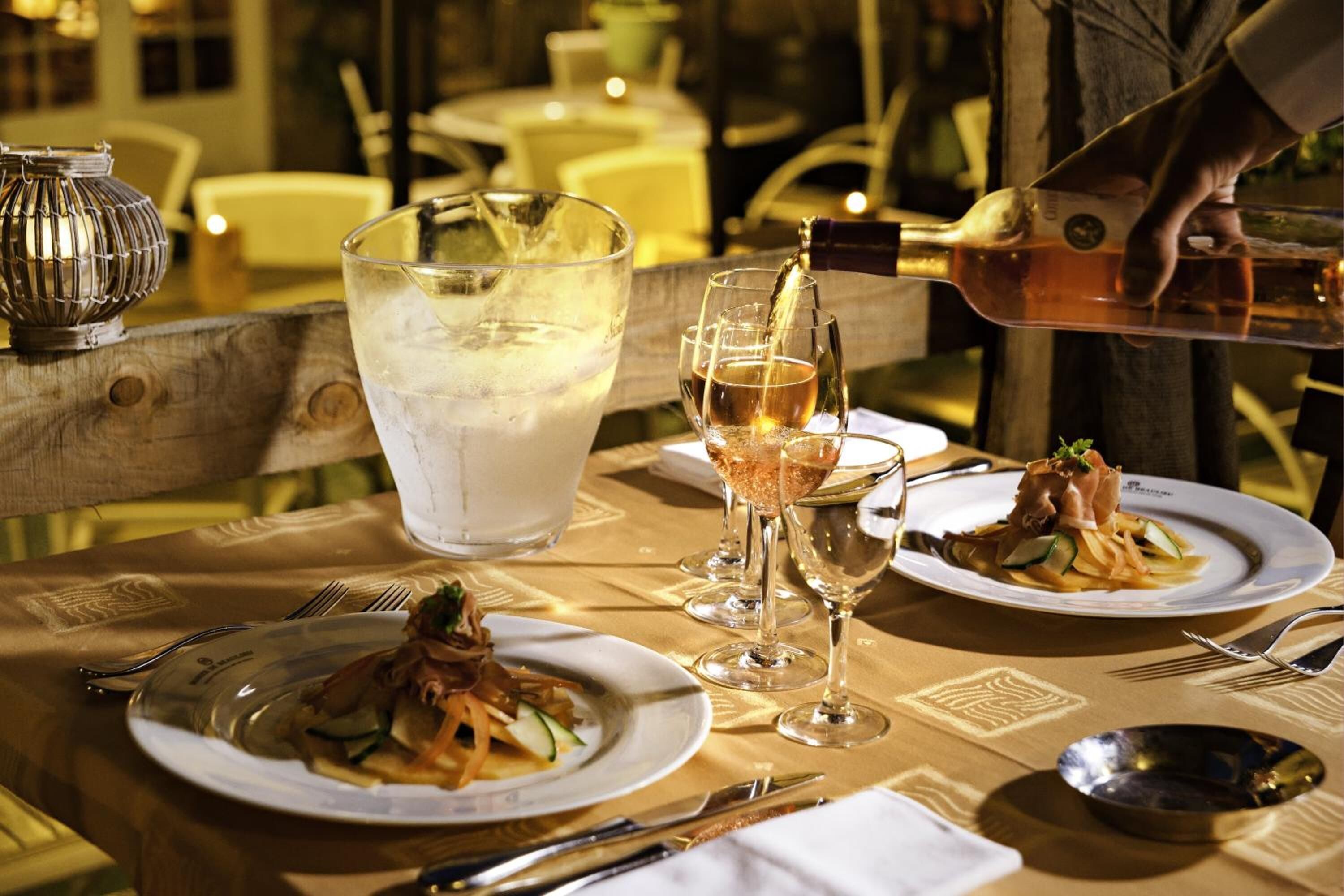 A dining table with plates of food, glasses of wine, and a large glass of water.