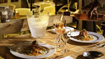 A dining table with plates of food, glasses of wine, and a large glass of water.