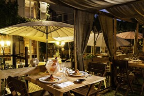 Un espace de restauration en plein air avec des tables et des chaises en bois, des parasols et des tables éclairées à la bougie.