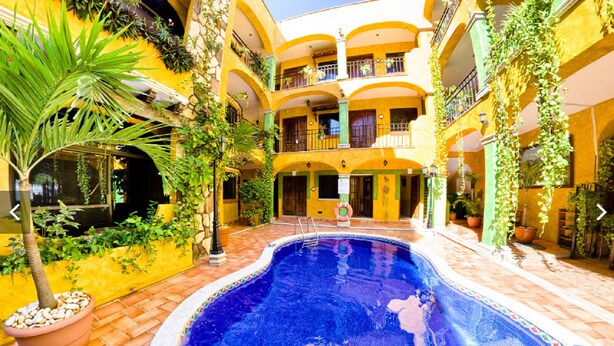 A courtyard with a swimming pool, potted plants, and a multi-story building with balconies.
