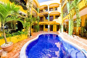A courtyard with a swimming pool, potted plants, and a multi-story building with balconies. - Hotel Hacienda Del Caribe (Playa del Carmen)