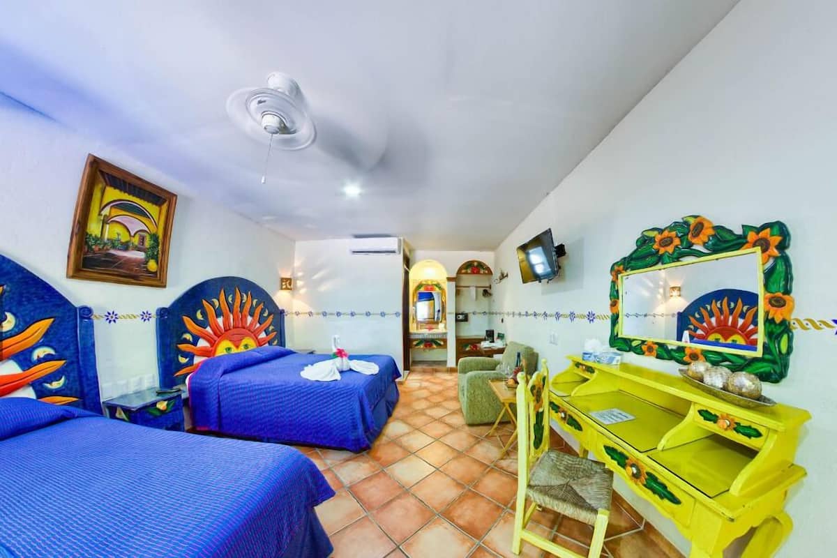 A hotel room with two beds, a yellow vanity, a mirror with a sunflower frame, and a painting on the wall.