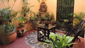 A courtyard with potted plants, a table, chairs, and a decorative wall.