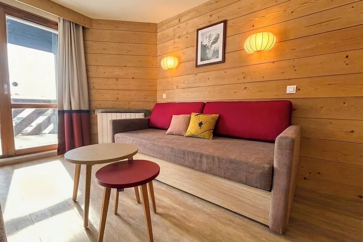 Um quarto com painéis de madeira, um sofá, duas luzes fixadas na parede, um quadro emoldurado e uma porta de vidro deslizante.