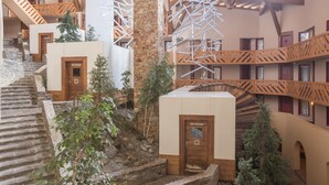 Hotelinterieur met meerdere niveaus, houten trappen, borden voor de ski-opbergruimte en een stenen muur.