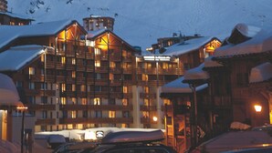 Berg bedekt met sneeuw in de schemering, met een hotel op de voorgrond met meerdere balkons en een verlichte gevel.