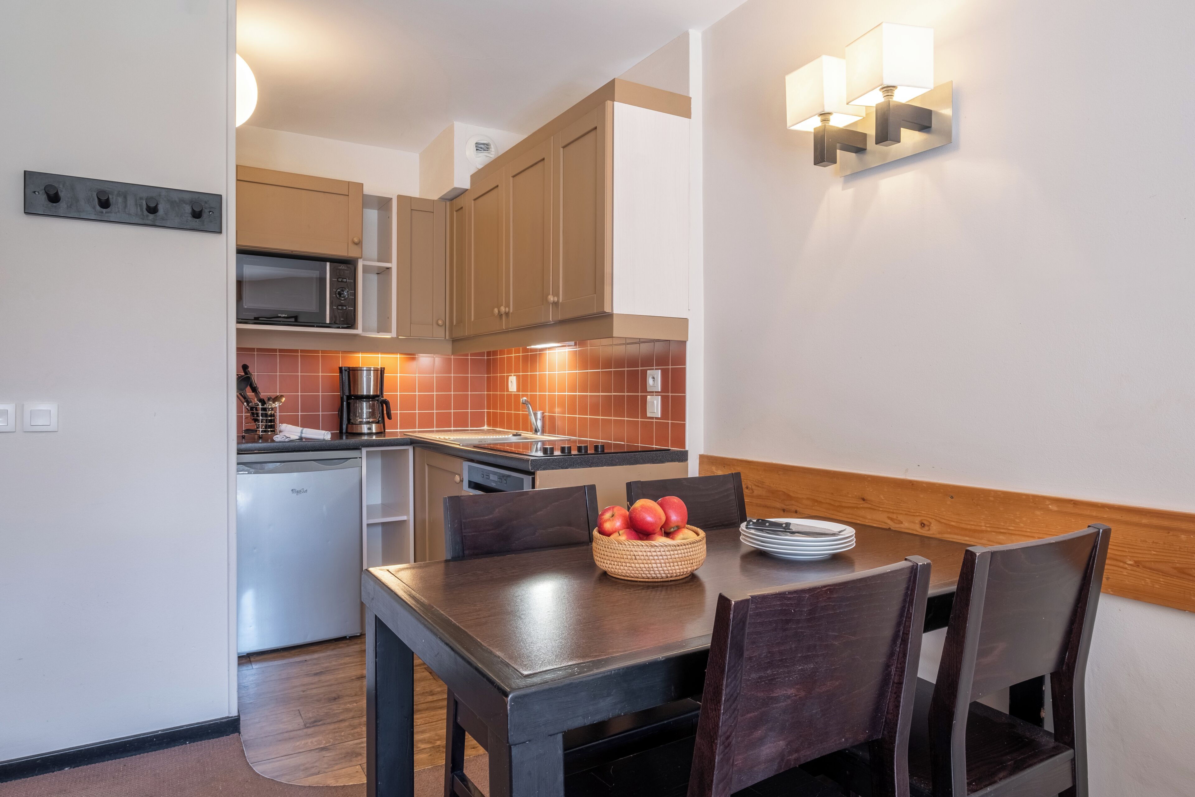 A compact kitchen with a dining area, a microwave, a coffee maker, and a fruit bowl on the table.