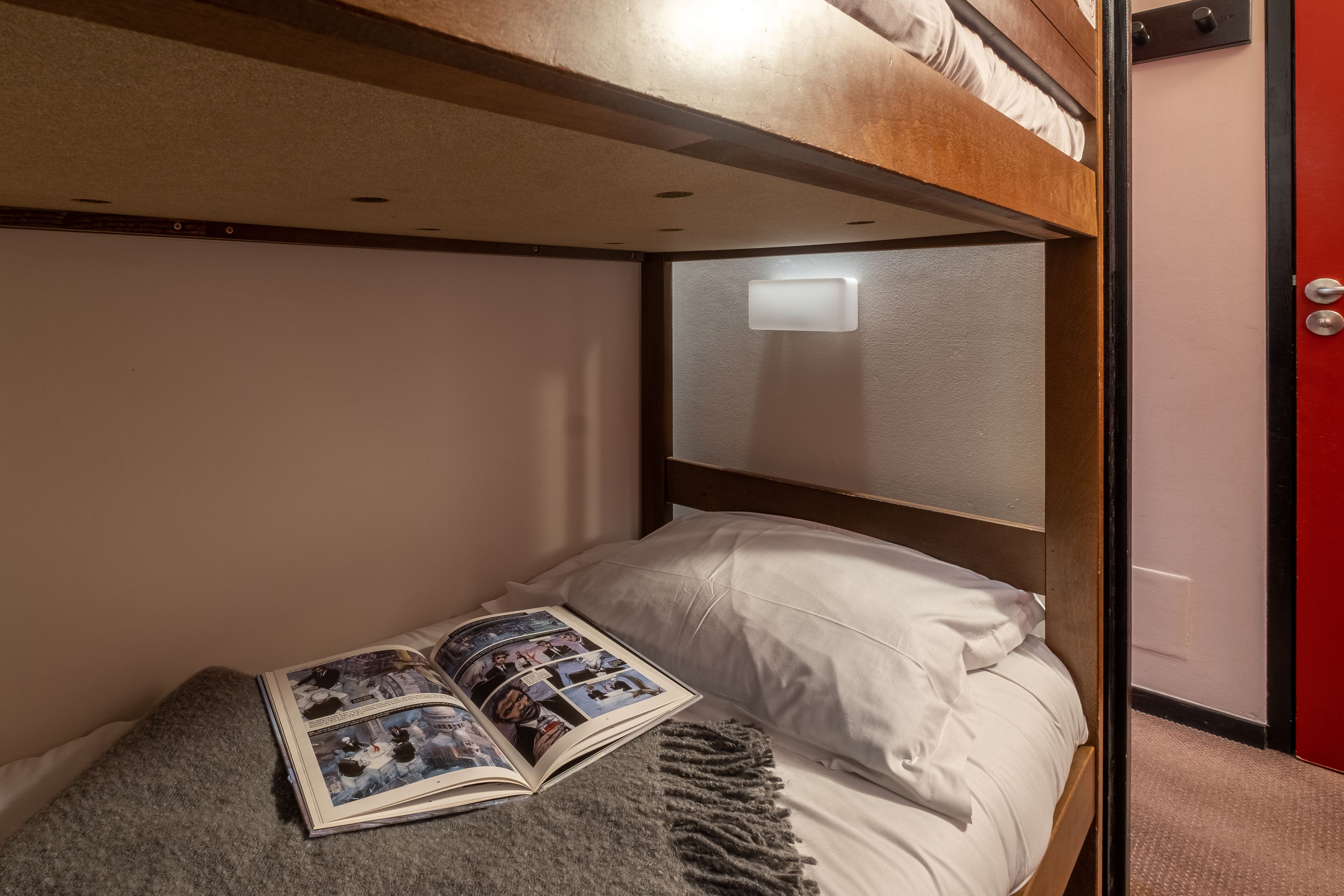 A bunk bed with a magazine on the lower bunk, a white pillow, and a grey blanket.