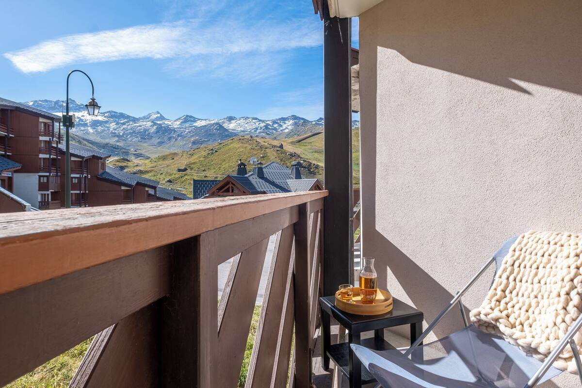 Uma varanda com vista para montanhas nevadas, uma mesa com uma bebida e uma cadeira.