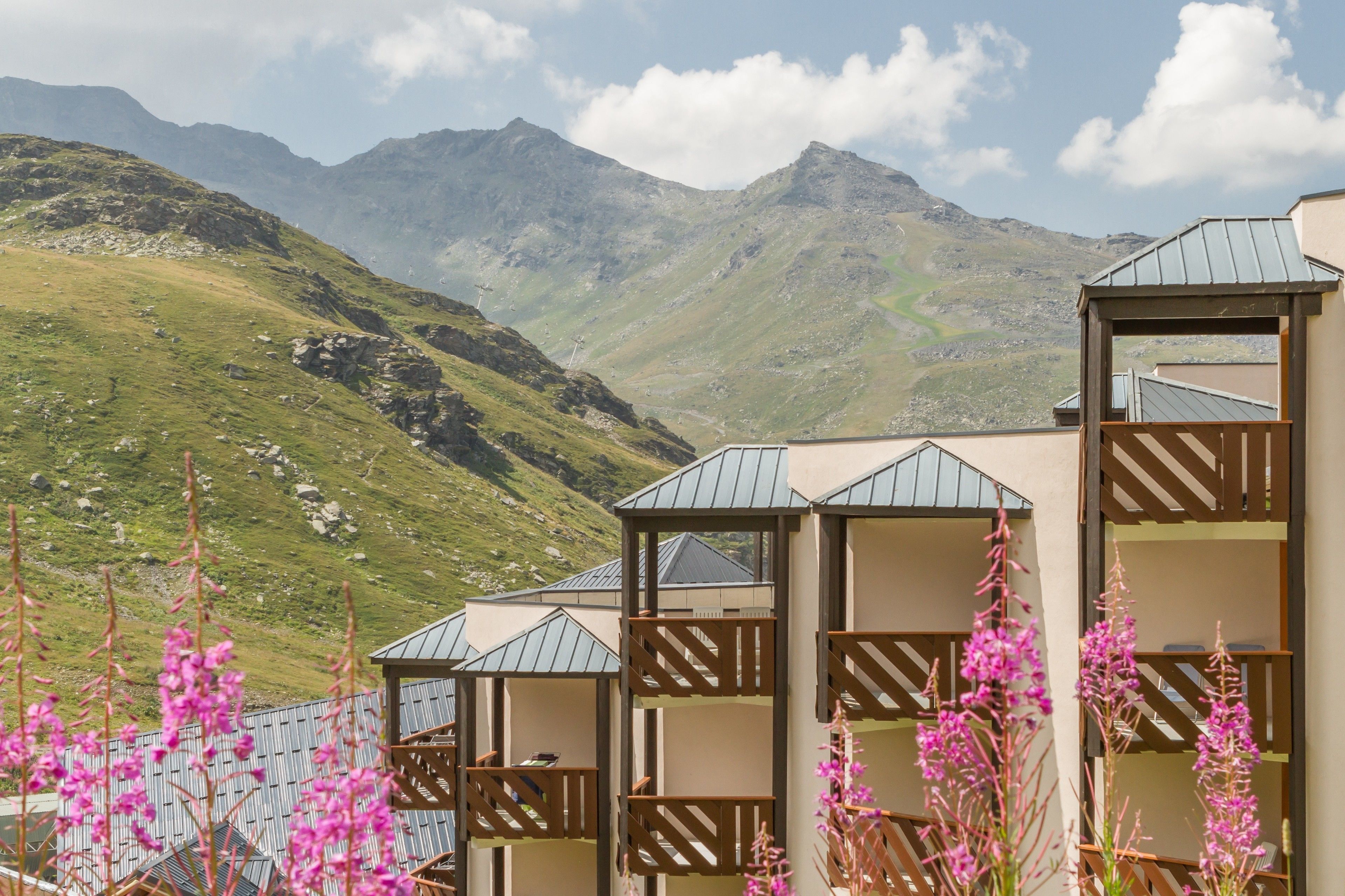 A mountain lodge with multiple rooms, each with a balcony and a view of the surrounding hills.