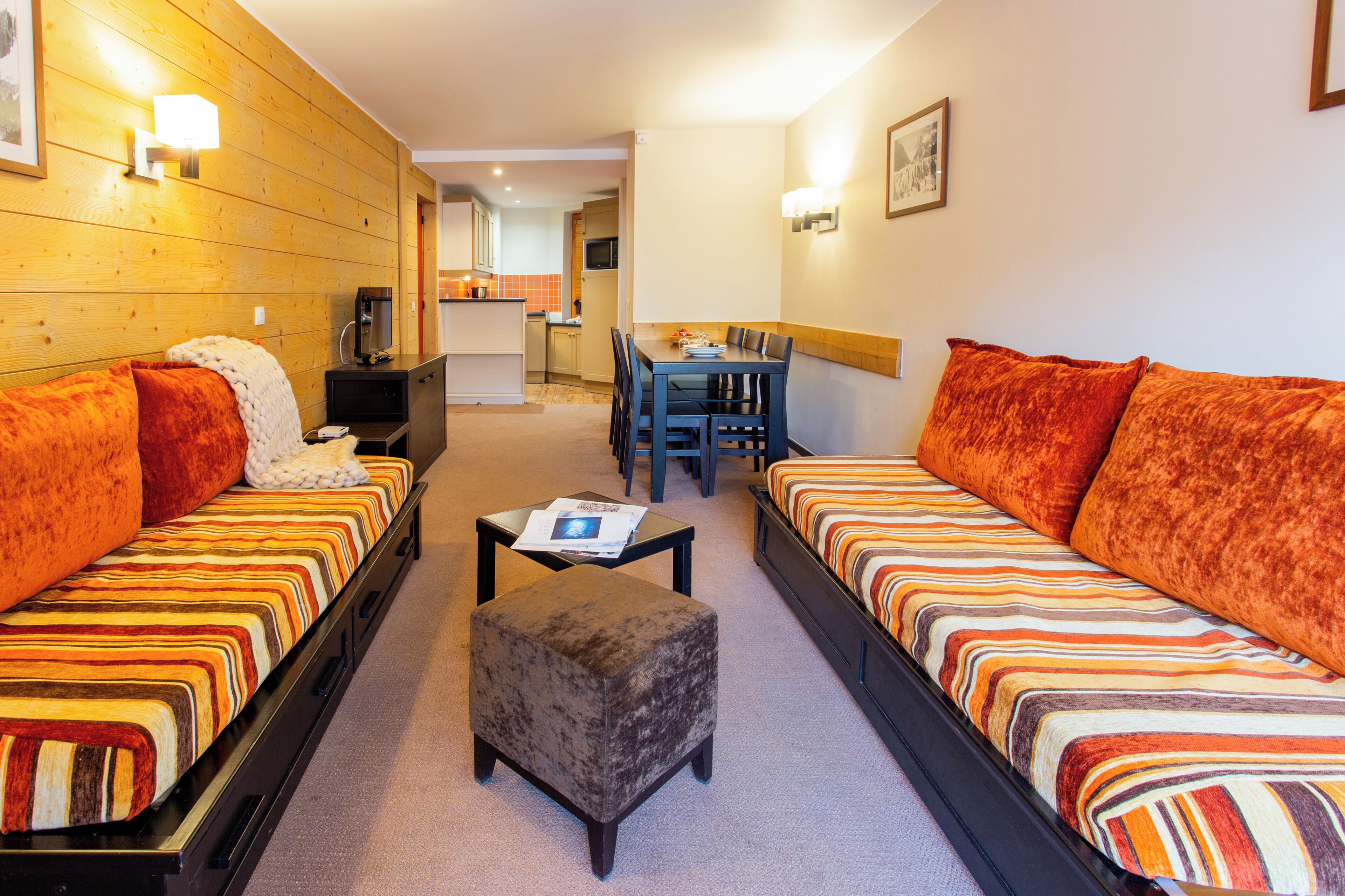 A hotel room with two sofas, a small ottoman, a dining table, and a kitchen area in the background.