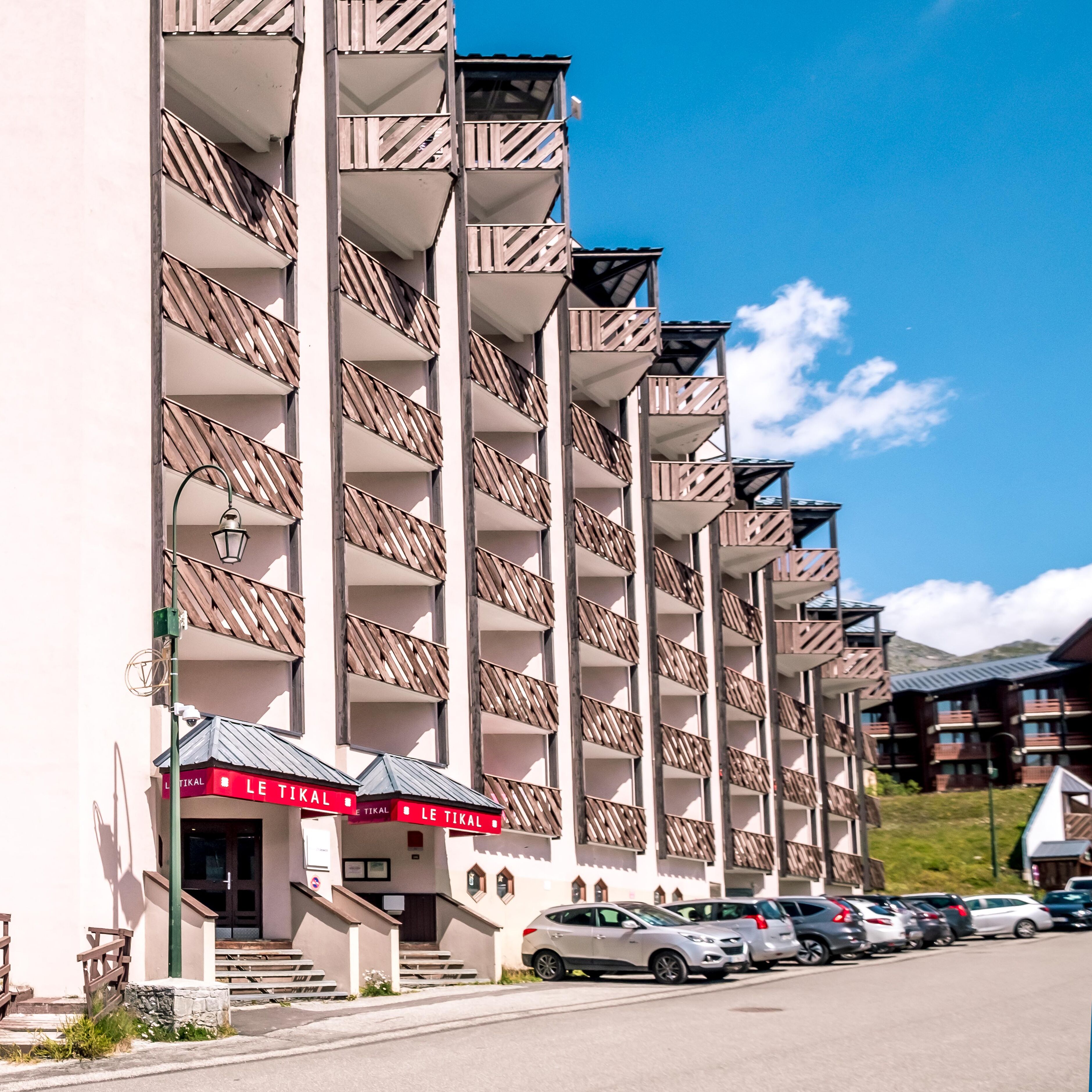 Ein mehrstöckiges Hotel mit Balkonen, einem Parkplatz und blauem Himmel.