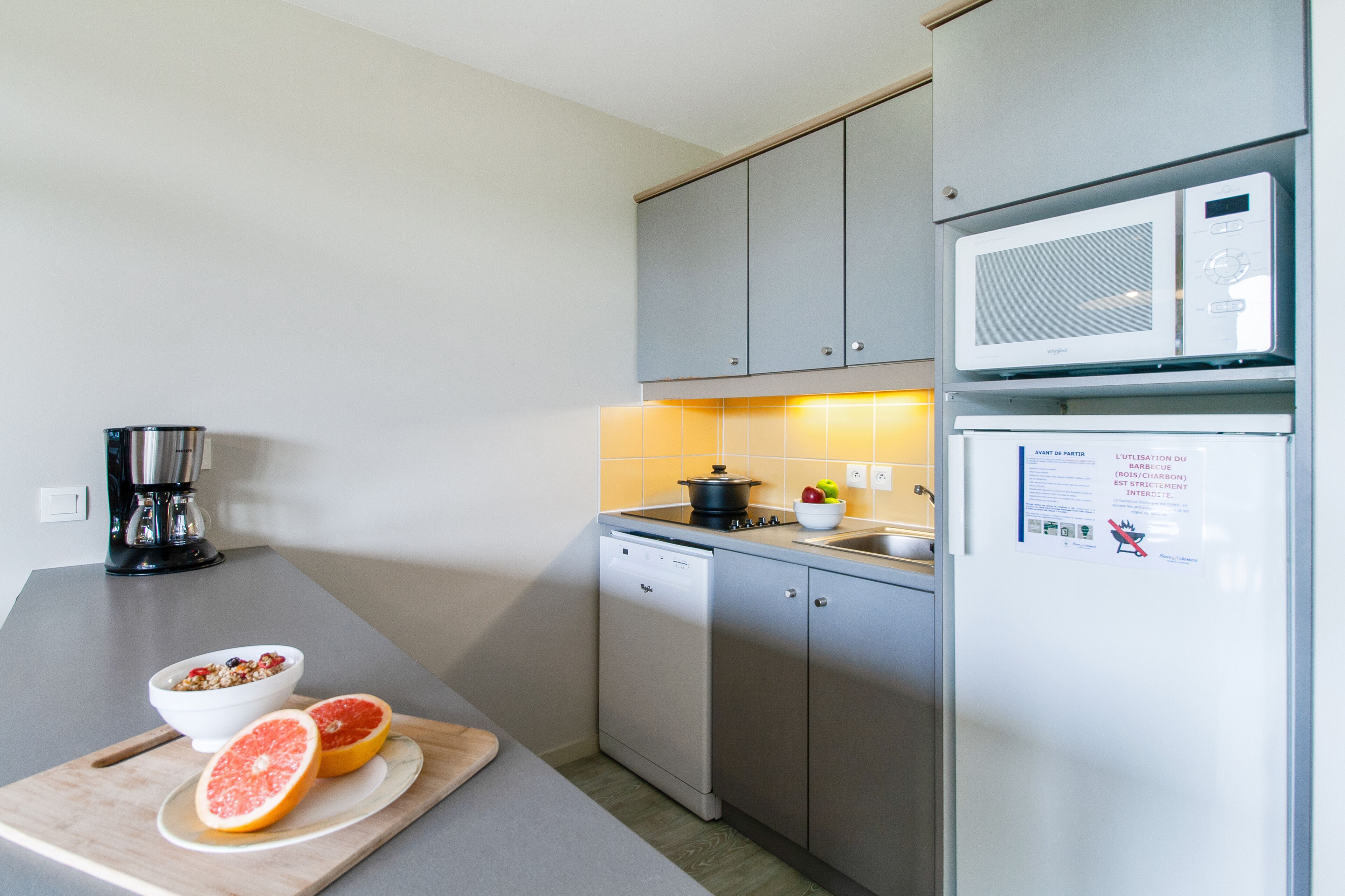 A modern kitchen with grey cabinets, a microwave, a dishwasher, and a cutting board with fruit.