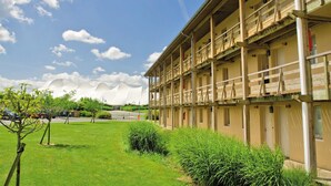 A multi-story building with balconies, a parking lot, and a grassy area with trees.