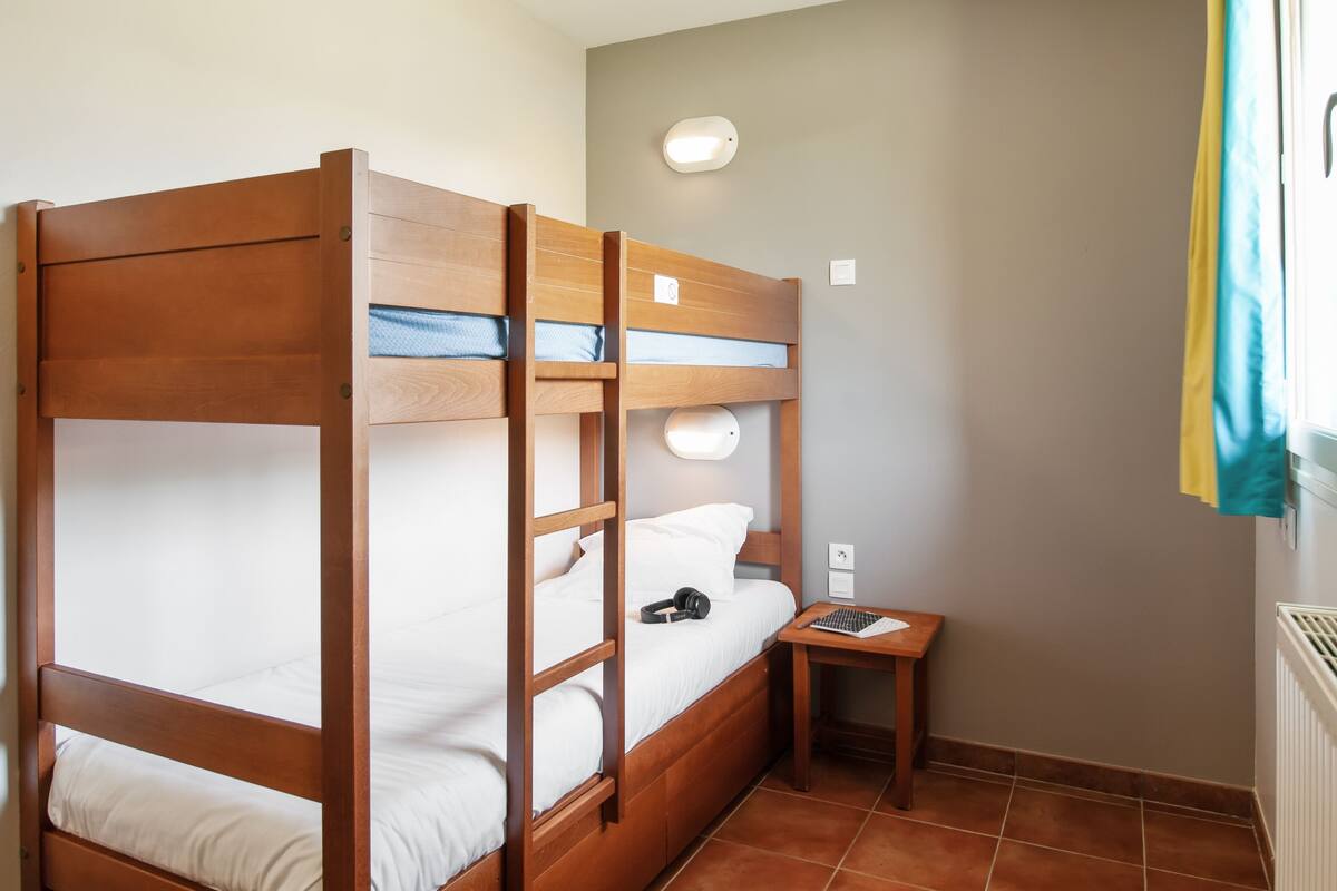 Une chambre avec un lit superposé en bois, une petite table de chevet et un luminaire fixé au mur.