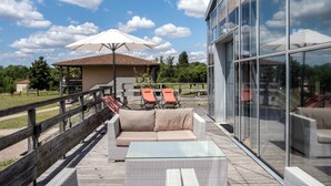 A deck with outdoor furniture, a glass-enclosed area, and a view of the surrounding landscape.