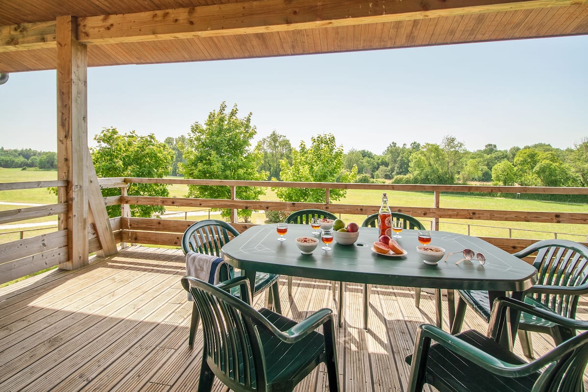 Une terrasse extérieure couverte, dotée d’un sol en bois, de chaises en métal vert et d’une table dressée pour le repas.