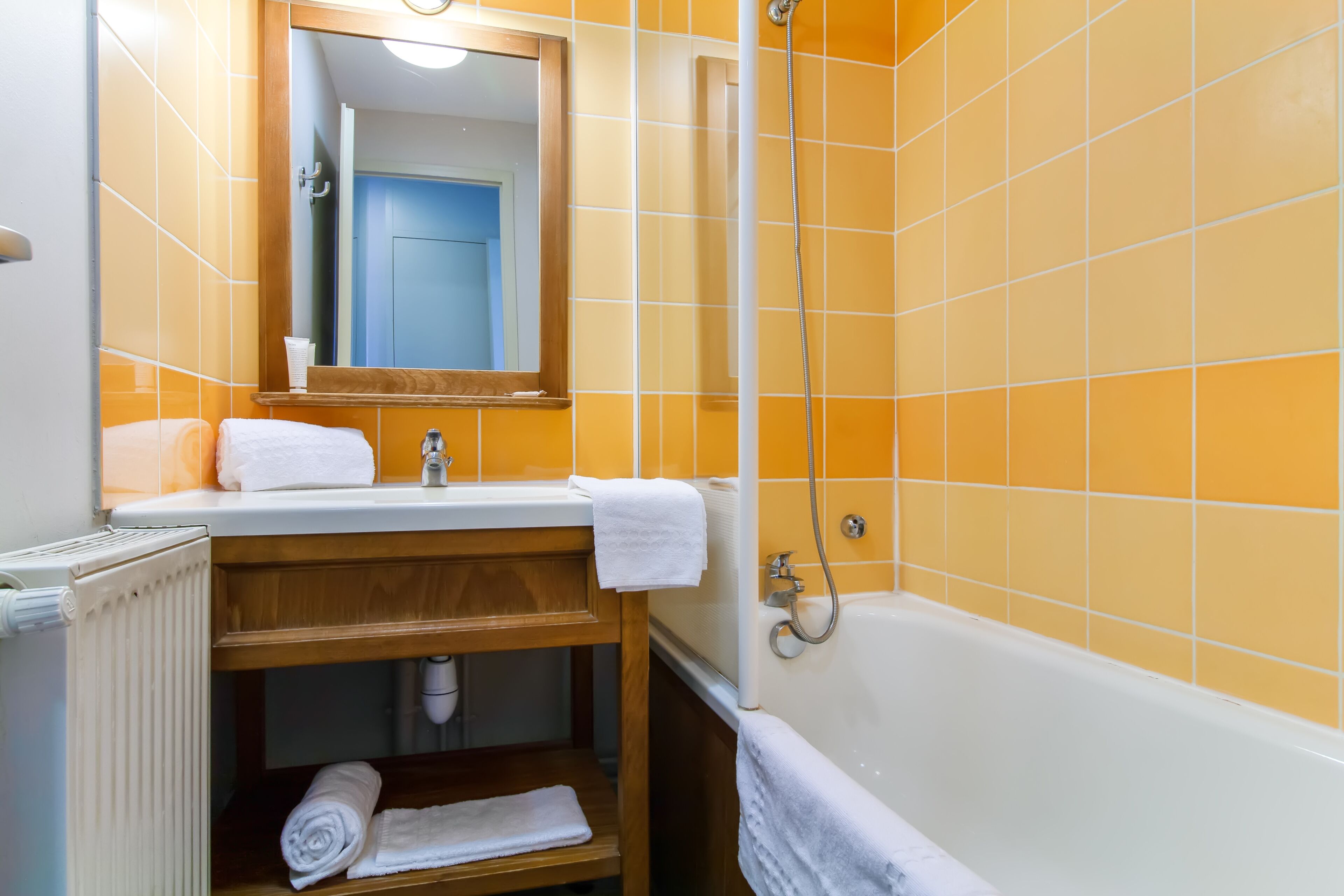 Un baño con azulejos naranja, una bañera blanca, un tocador de madera y un espejo sobre el lavabo.