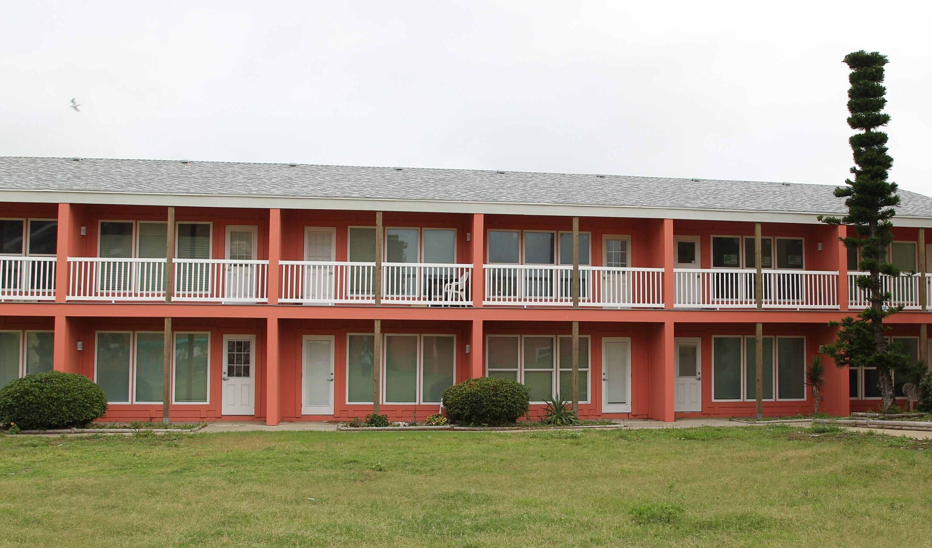 A multi-story motel with a red exterior, white balconies, and a grassy front yard.