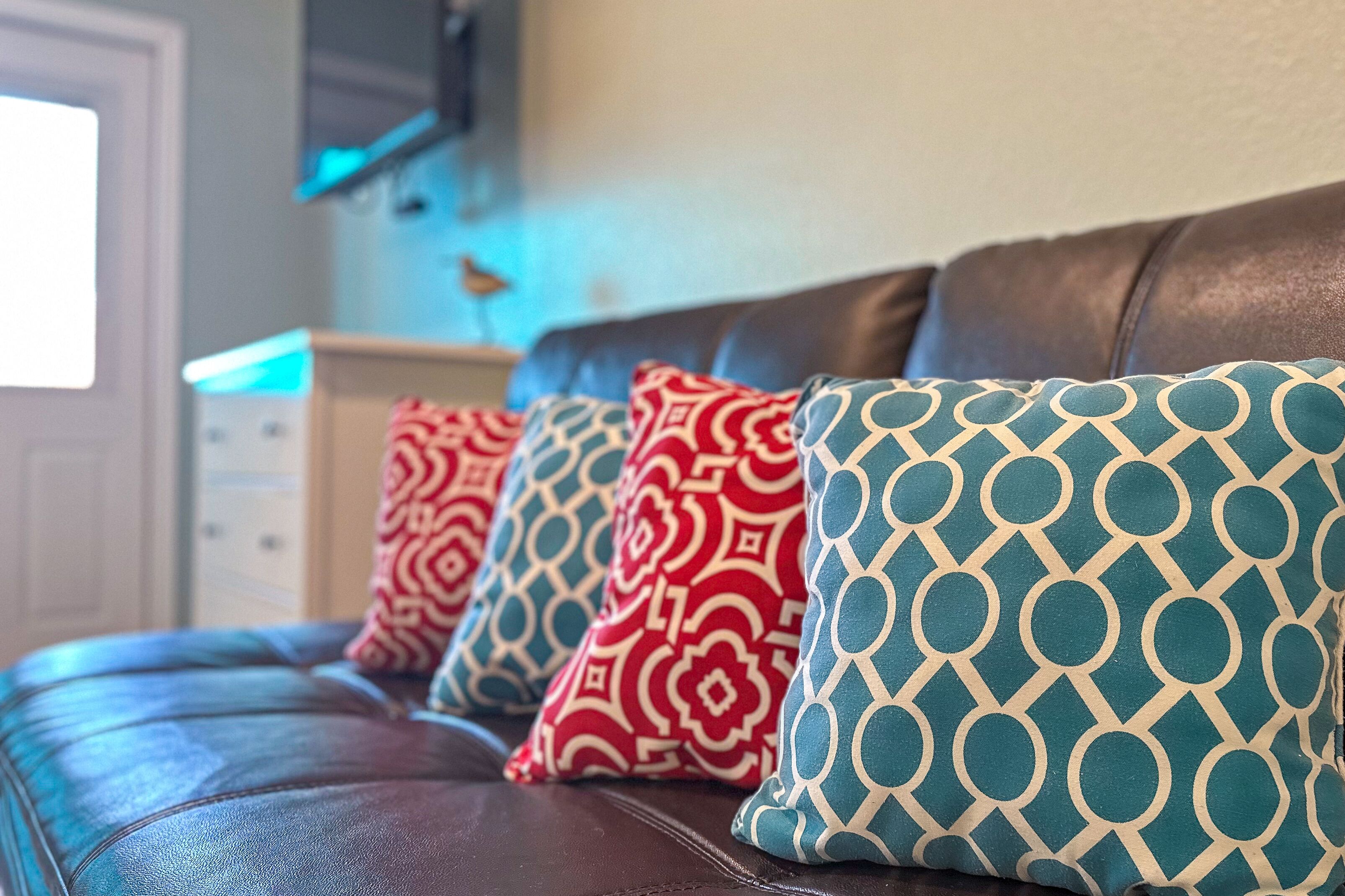 A brown leather sofa with patterned cushions in red and blue.
