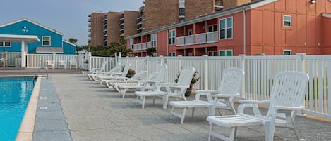 A poolside area with white lounge chairs and a blue building in the background.
