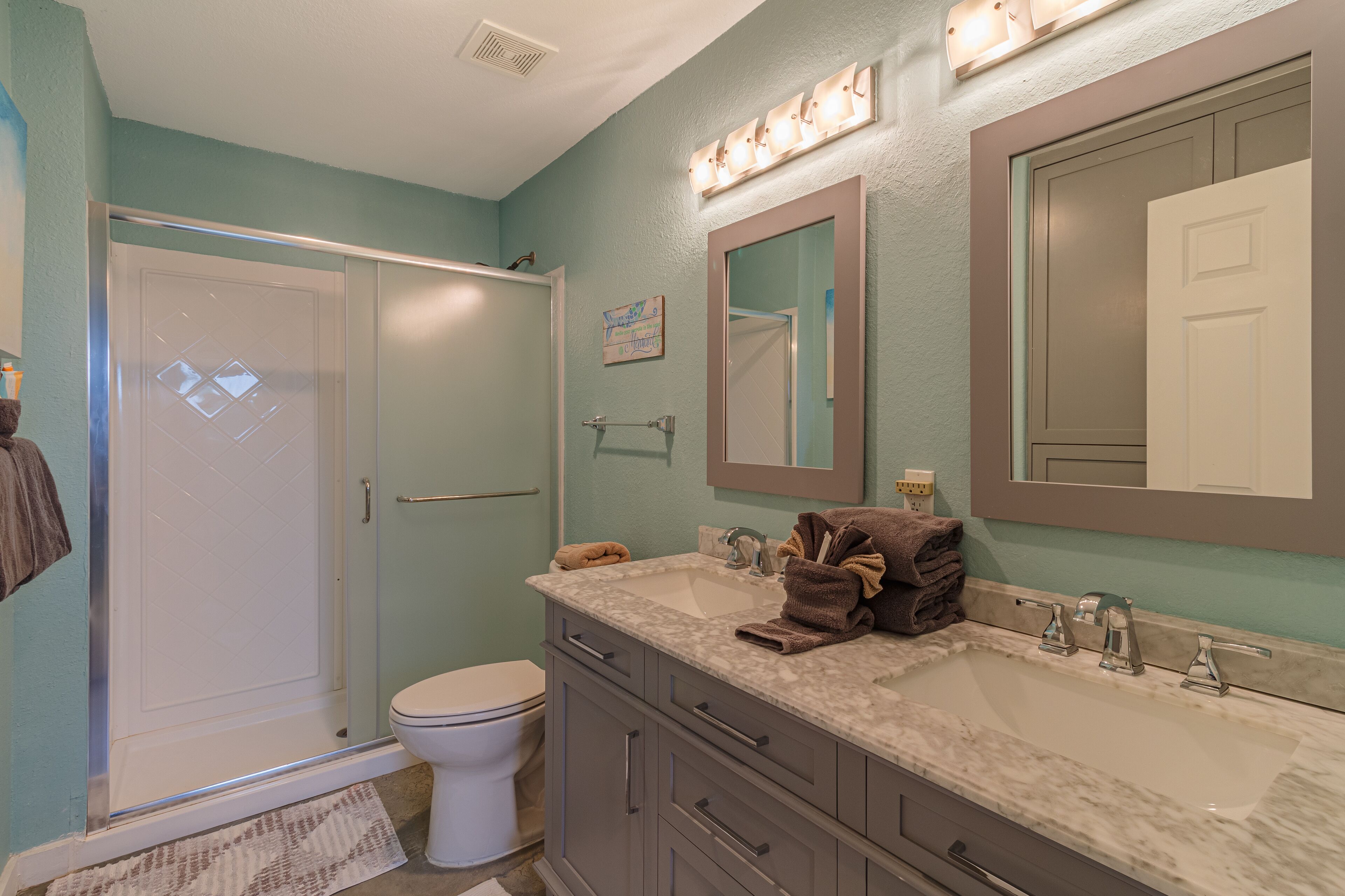 A bathroom with a shower, toilet, vanity, and mirrors.