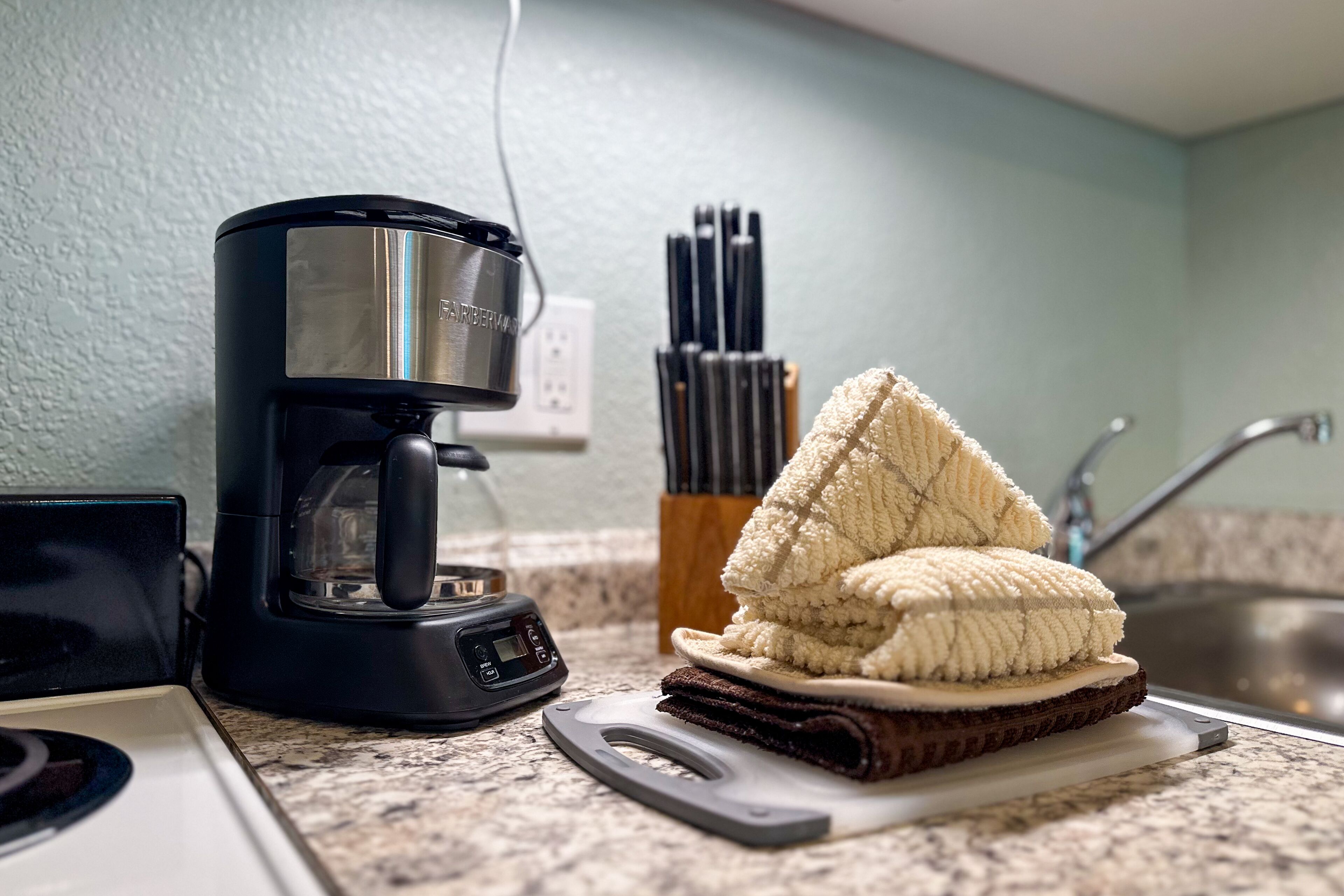 A kitchen with a coffee maker, a stack of towels, and a knife block.