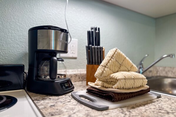 A kitchen with a coffee maker, a stack of towels, and a knife block.