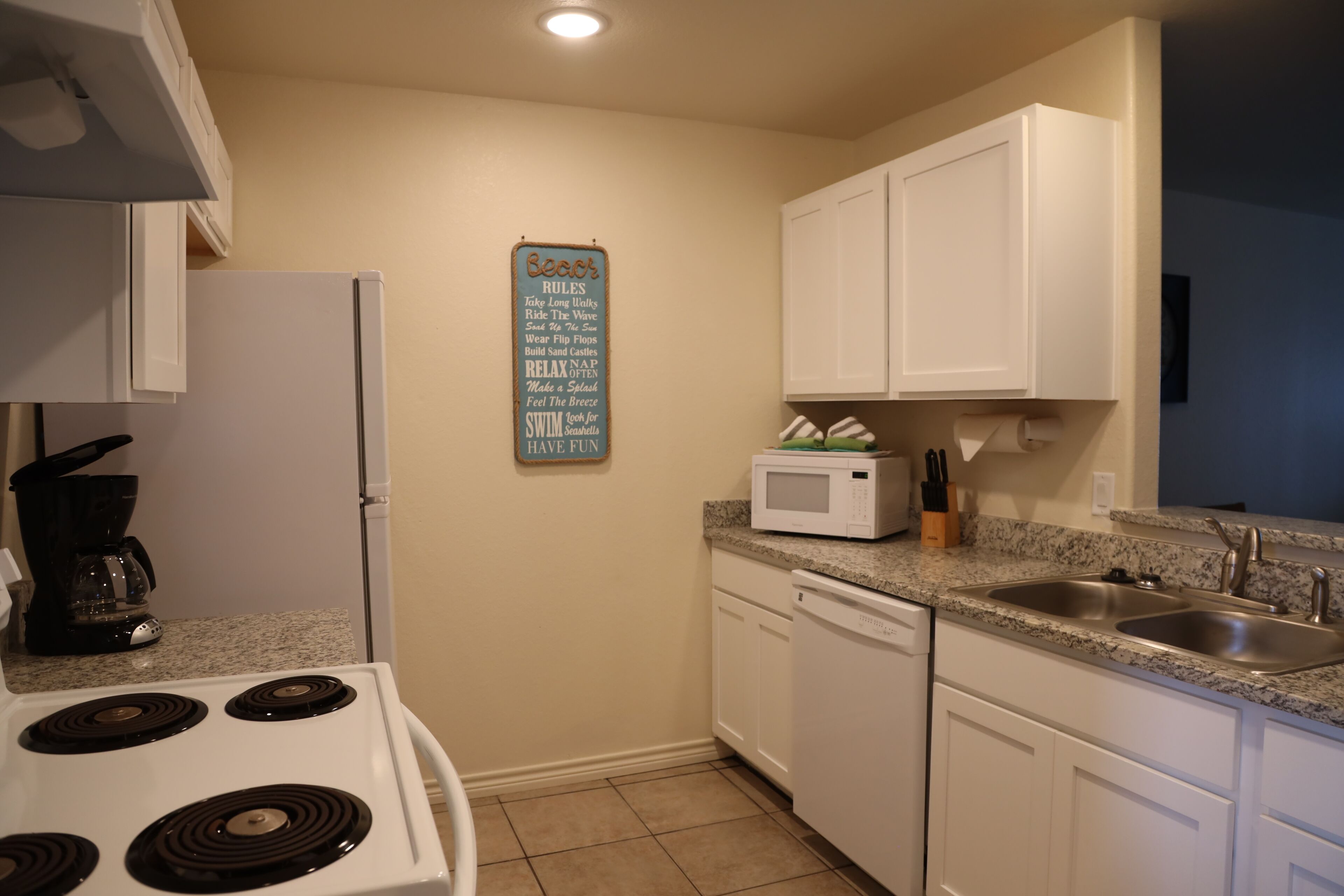A kitchen with white cabinets, a stove, a microwave, and a sink.