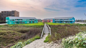 A coastal hotel with a wooden boardwalk leading to a grassy lawn and beach. - Executive Keys Condominiums on the Beach (Port Aransas)