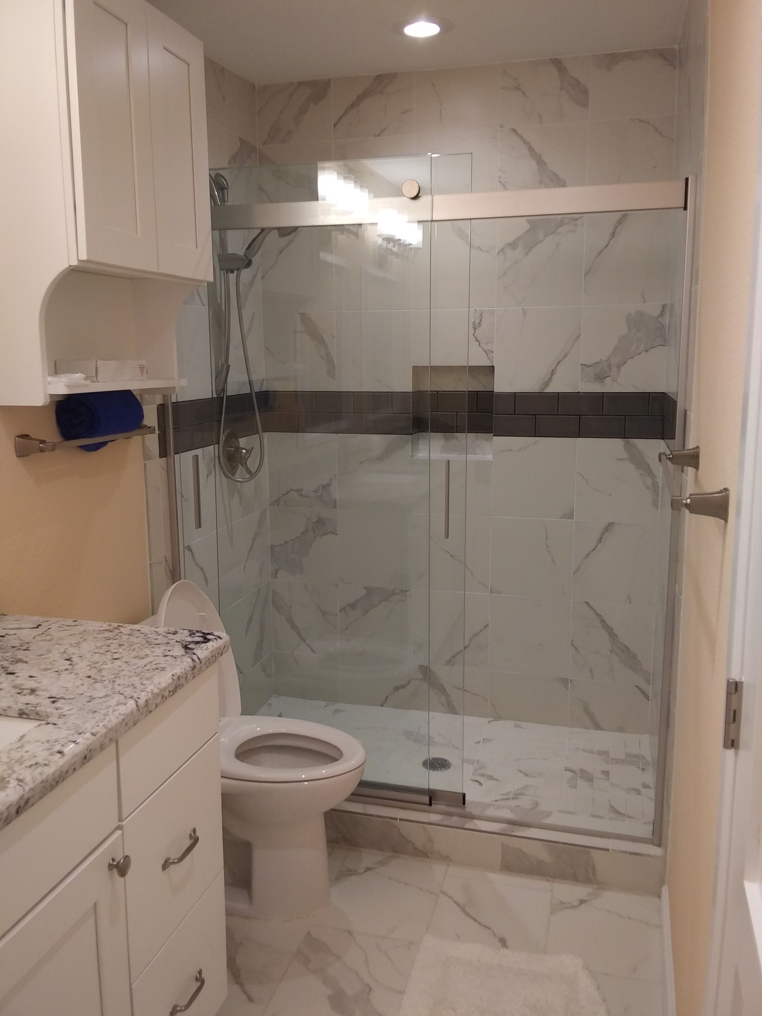 A bathroom with a toilet, a shower enclosure, marble tiles, and a white countertop.