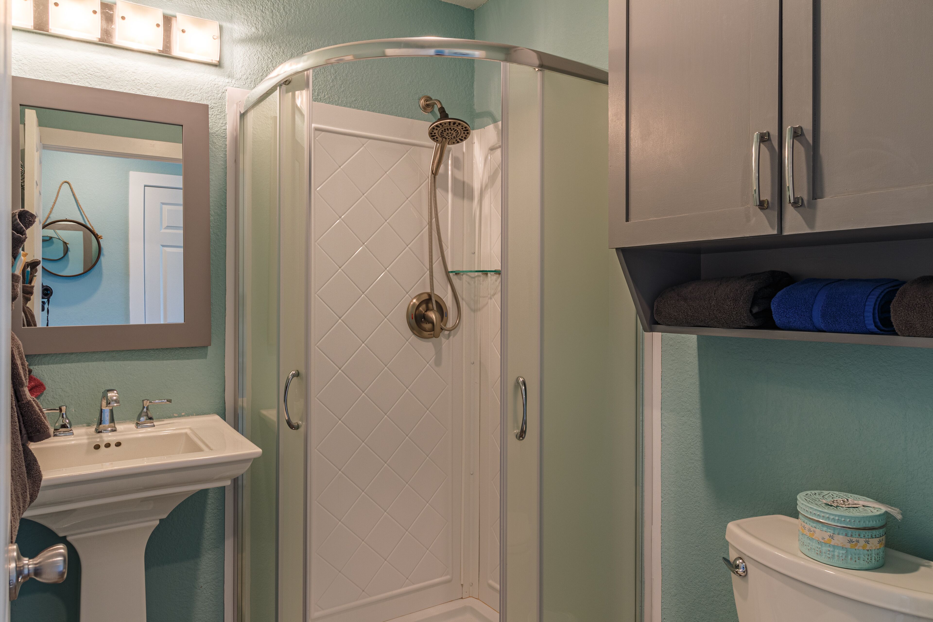 A bathroom with a shower, sink, toilet, and cabinets.