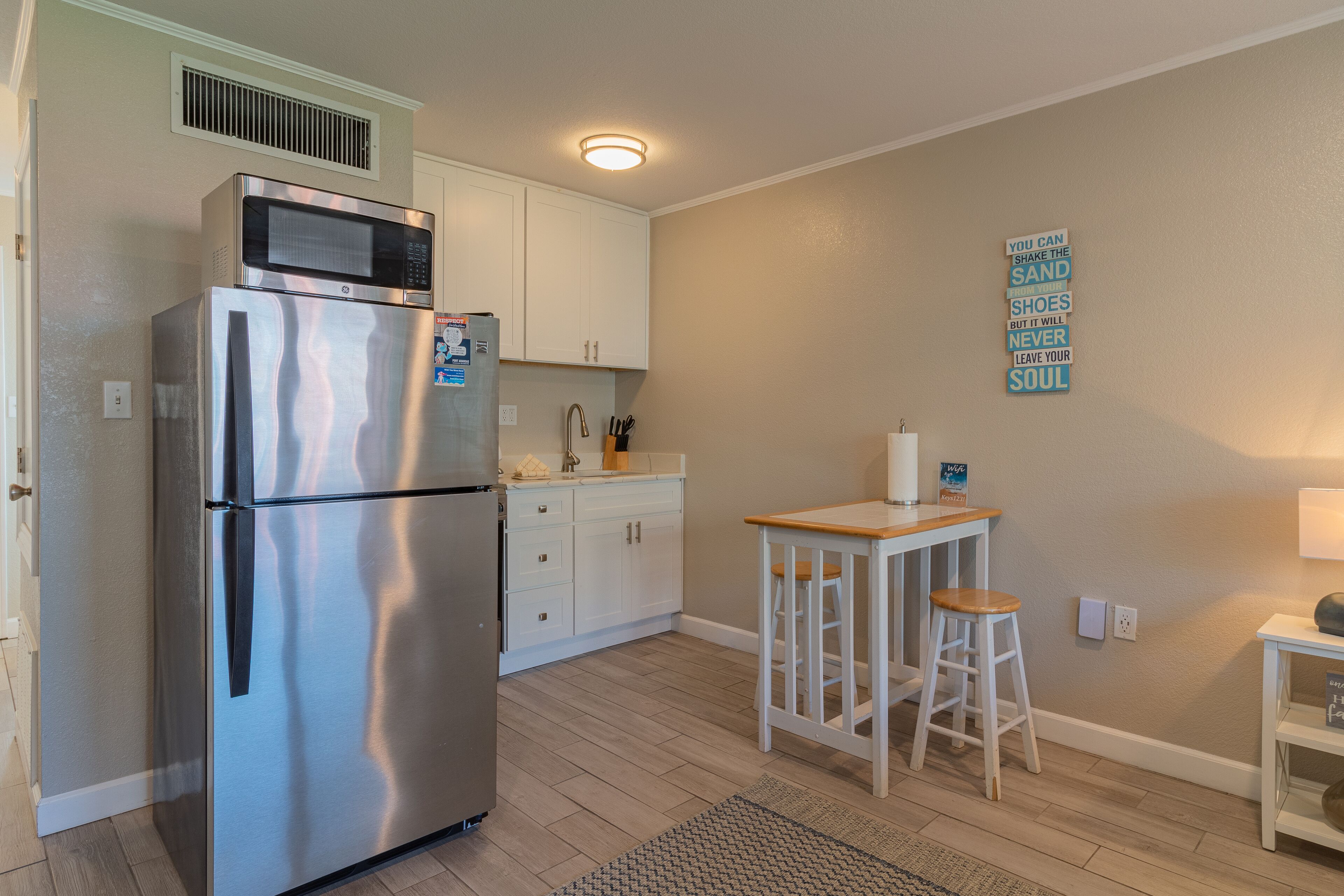 A kitchen with a stainless steel refrigerator, white cabinets, a wooden countertop, and a small bar area with stools.