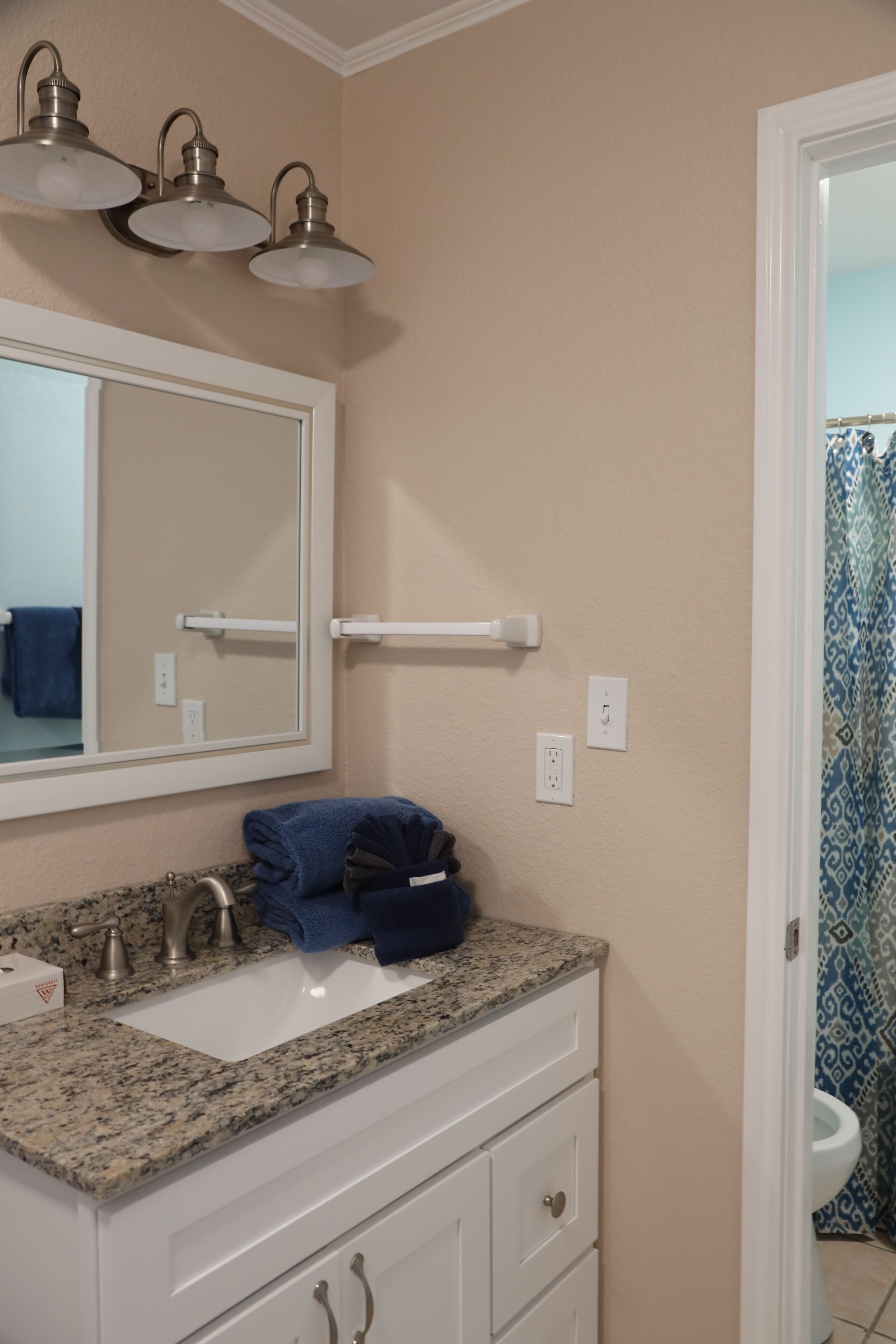 A bathroom with a sink, mirror, towel rack, and a toilet visible through an open door.