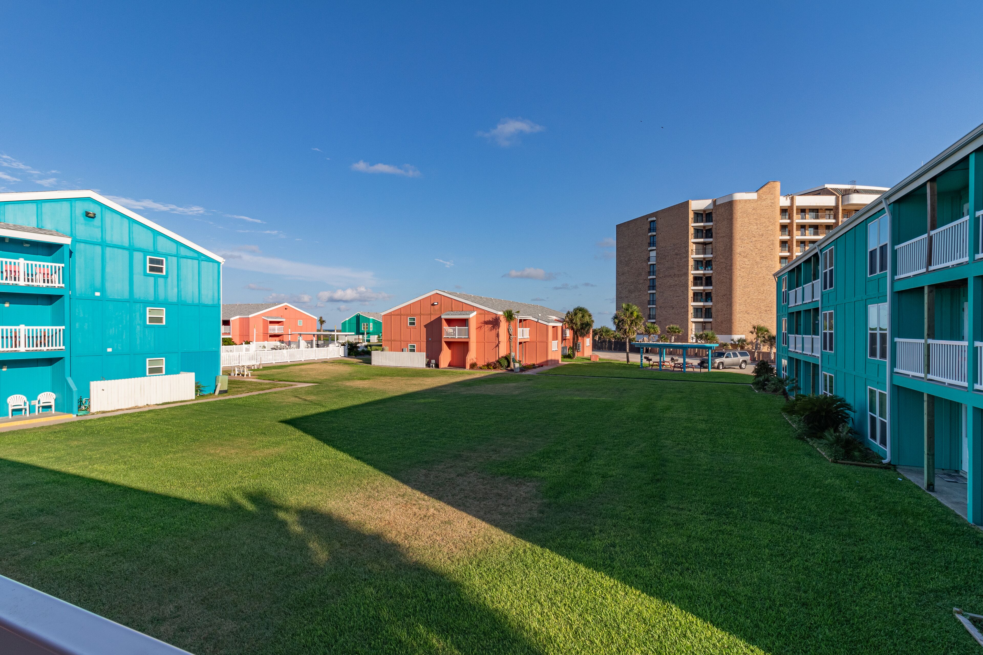 Un barrio residencial con un césped verde, un edificio rojo y un edificio azul con balcones.