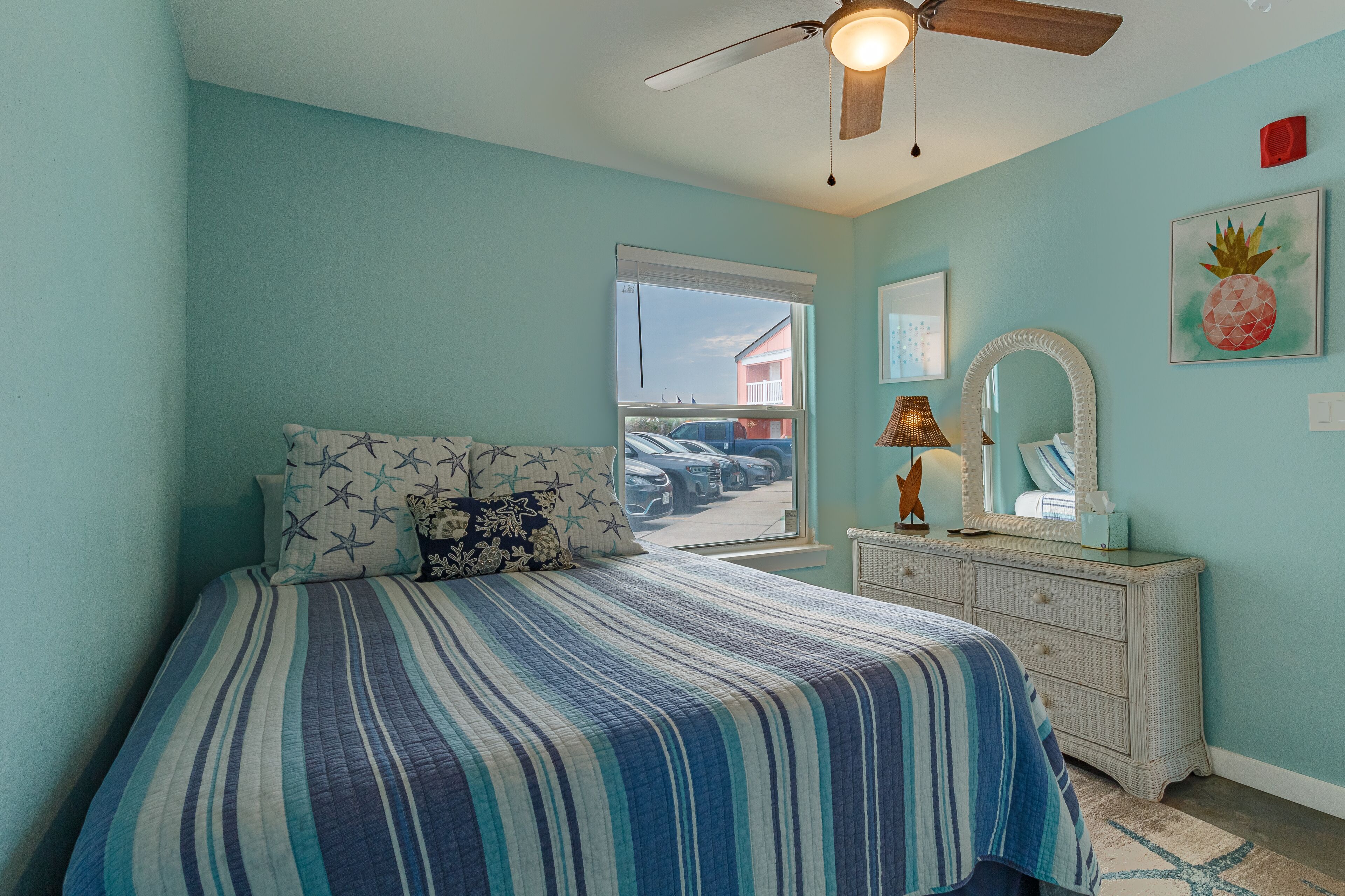 A bedroom with a bed, a dresser, a ceiling fan, a window, and a door leading outside.