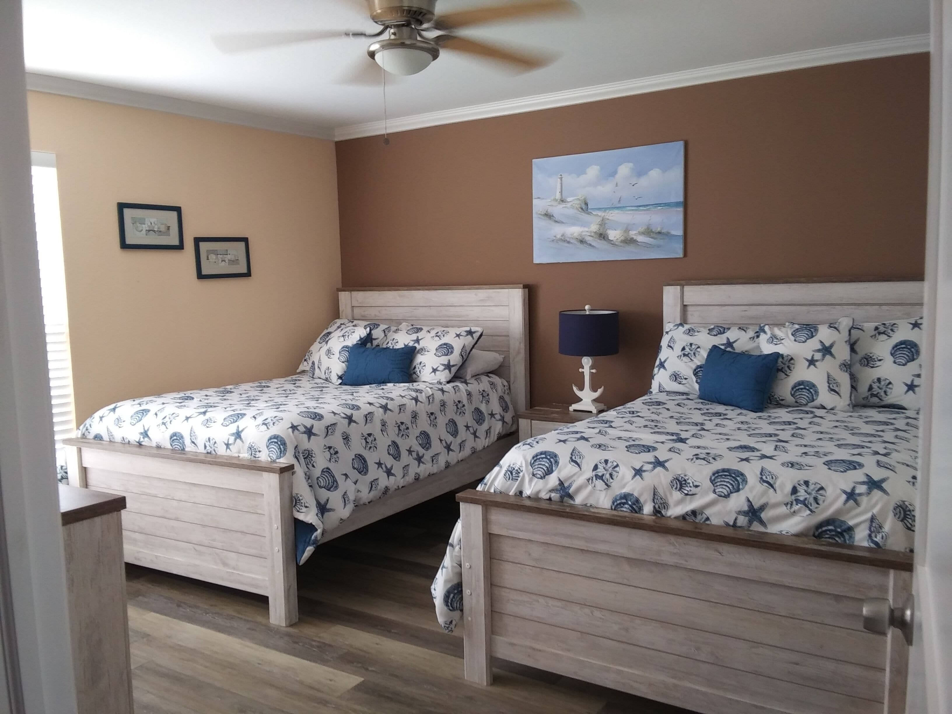 Une chambre avec deux lits, un ventilateur de plafond, un tableau et des photos encadrées accrochées au mur.
