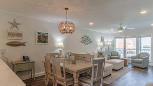 A dining area with a wooden table and chairs, a chandelier, and artwork on the walls. - Executive Keys Condominiums on the Beach (Port Aransas)