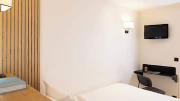 Habitación de hotel con pared de listones de madera, una cama, un escritorio con una silla, un televisor montado en la pared y una mesita de noche con un libro.