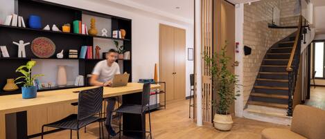 A modern living room with a wooden desk, black chairs, and a bookshelf filled with books and decorative items.
