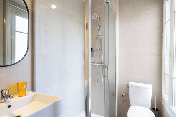 Un baño moderno con ducha envuelta en vidrio, un lavabo blanco y un inodoro.
