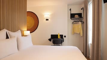 Habitación de hotel con una cama grande, un escritorio con silla, estante en la pared con un sombrero y una ventana con cortinas.