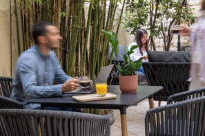 A person using a laptop at an outdoor table with a potted plant and a glass of orange juice. - Korner Montmartre (Paris)