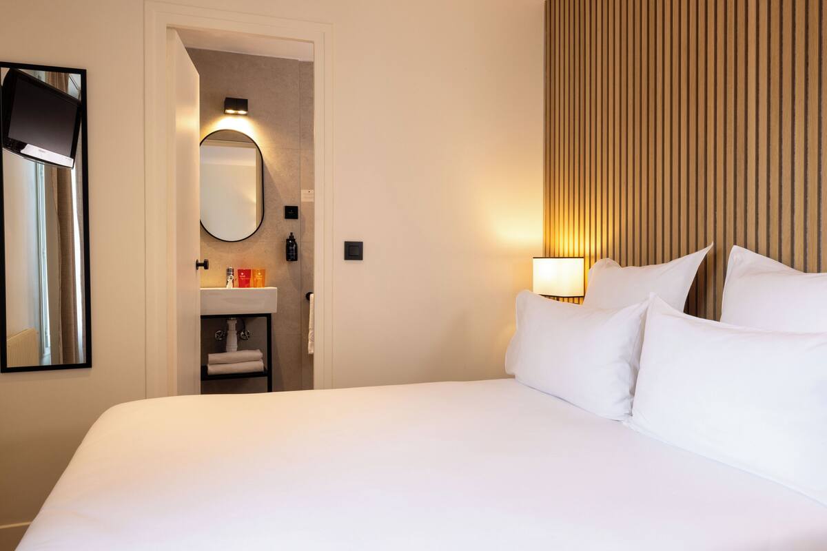 A hotel room with a large bed, a bedside lamp, a mirror, and a bathroom visible through an open door.
