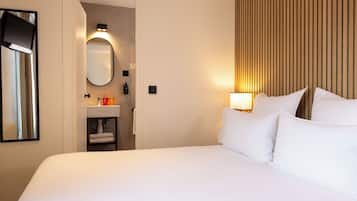 Habitación de hotel con una cama grande, una lámpara de noche, un espejo y un baño visible a través de una puerta abierta.