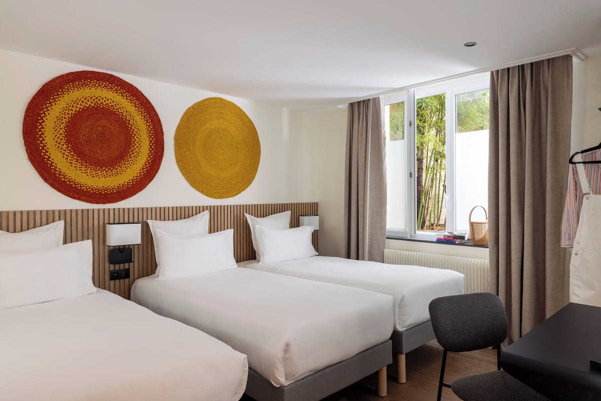 A hotel room with two beds, a desk, a chair, and a large window with curtains.