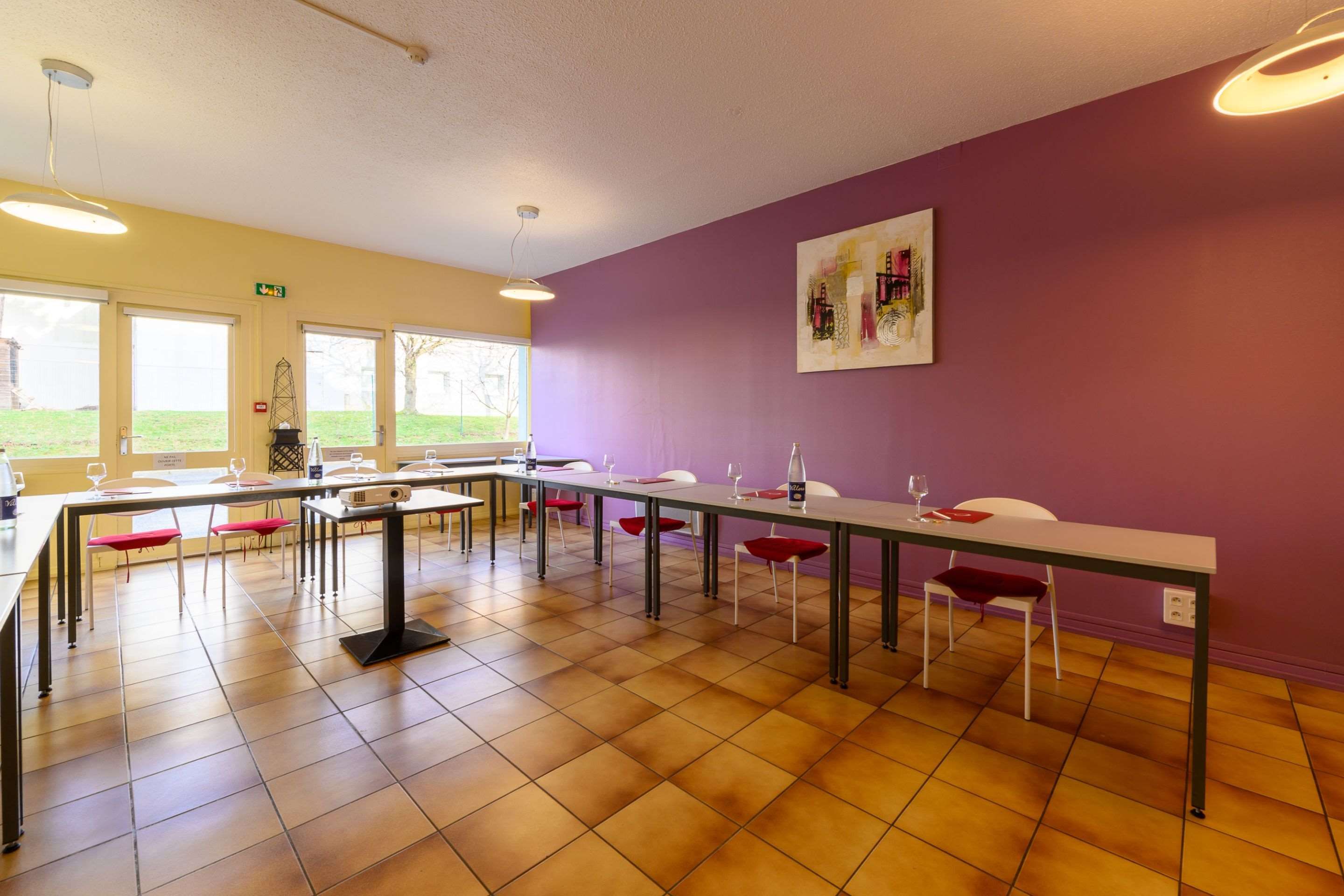 Un salón de conferencias con una larga mesa, sillas, un proyector y un cuadro en la pared.