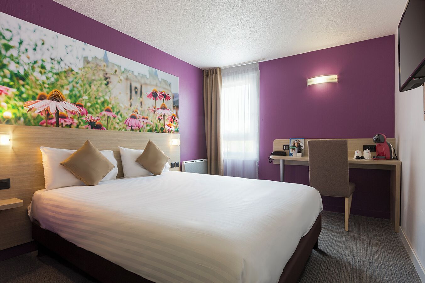 A hotel room with a bed, a desk, a chair, a painting, and a television.